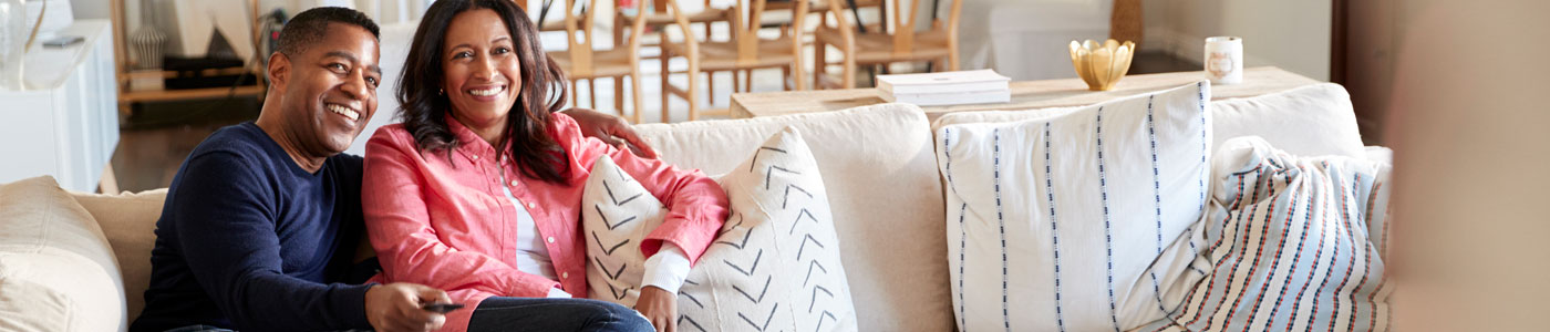 Middle aged couple on couch smiling and watching TV