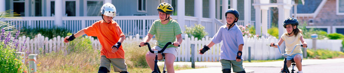 Four young kids playing in the street, riding bikes and roller skating.